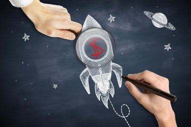 Male hands drawing and holding magnifier over space ship sketh with red dollar sign. Chalkboard background. Start up concept clipart