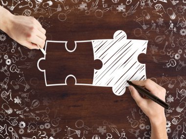 Male hands drawing puzzle pieces and success icons sketch on wooden desktop. Business partnership concept clipart