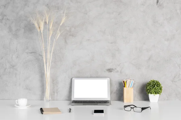 Креативный дизайнерский рабочий стол с чистым белым ноутбуком, смартфоном, очками, блокнотом, кофейной чашкой, красочными карандашами и растением на бетонном фоне стены. Mock up — стоковое фото