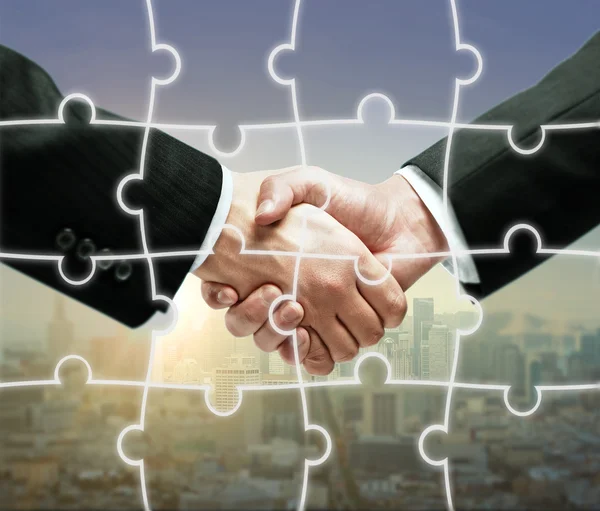 Businesspeople shaking hands on city background with puzzle piece pattern.