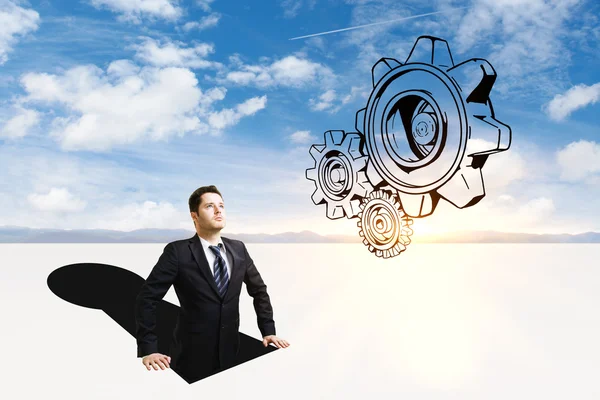 Businessman inside abstract keyhole looking at cogwheel sketch on sky background. Teamwork concept — Stock Photo, Image