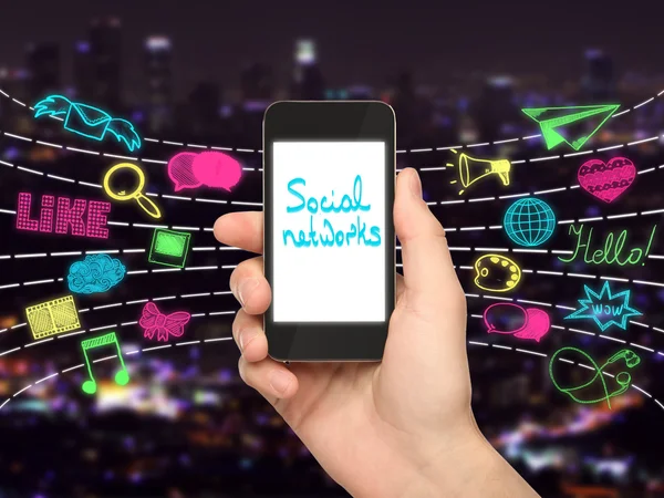 Hand houden smartphone met tekst op het scherm en kleurrijke media iconen op de achtergrond van de stad. Sociale netwerken concept — Stockfoto