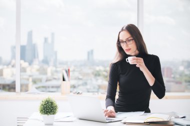 Laptop kullanan, kahve içen bir kadın.