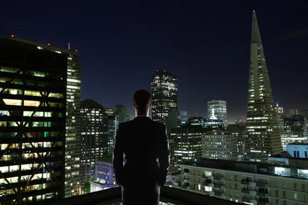 屋上のビジネスマンは、照らされた夜の街を見て。研究コンセプト — ストック写真