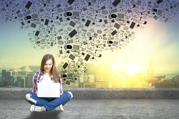 Menina hipster sorridente no telhado usando laptop com ícones de mídia abstratos acima no fundo da cidade. Conceito de redes sociais — Fotografia de Stock