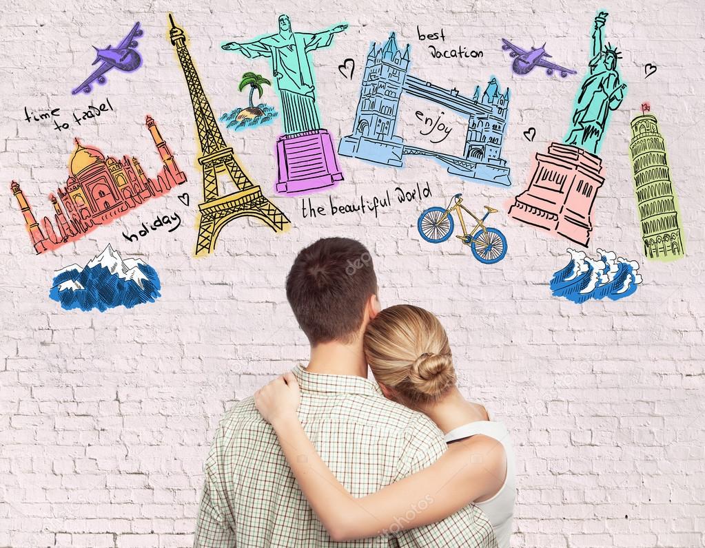 Young caucasian couple looking at creative travel sketch on brick background. Traveling concept