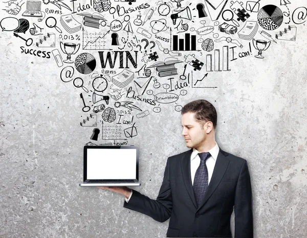 Young businessman in suit holding blank white laptop on concrete background with creative business sketch. Mock up, Success concept — Stock Photo, Image