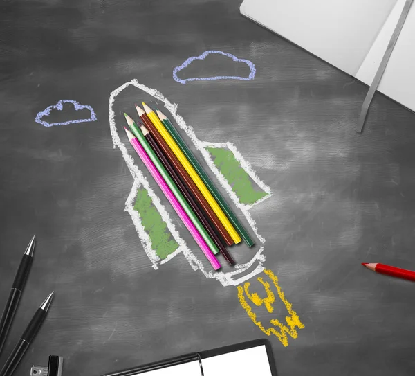 Abstract rocket ship sketch around colorful pencils on chalkboard surface with other supplies. Education concept — Stock Photo, Image