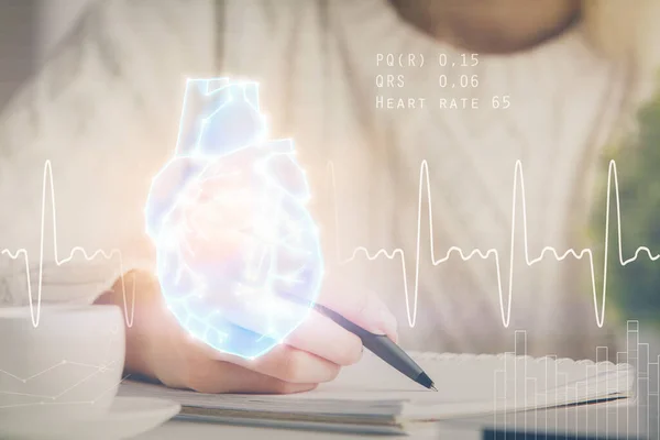 Holograma del corazón sobre las manos de las mujeres escribiendo fondo. Concepto de estudio médico. Exposición múltiple — Foto de Stock