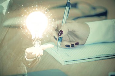 El üstünde tutulan ampul hologramı notlar alıyor. Fikir kavramı. Çift pozlama