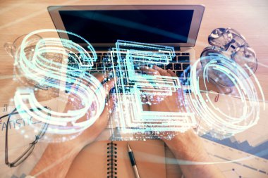 Bilgisayar klavyesinin ve SEO hologram çiziminin üzerine yazı yazan bir adamın eline çok kez maruz kalmış. Üst Manzara. Arama optimizasyon kavramı.