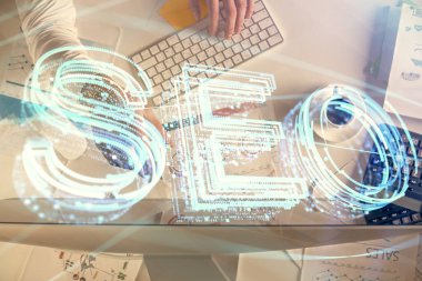 Bilgisayar klavyesinin ve SEO hologram çiziminin üzerine yazı yazan bir adamın eline çok kez maruz kalmış. Üst Manzara. Arama optimizasyon kavramı.