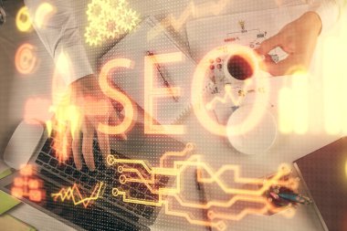 Bilgisayar klavyesinin ve SEO hologram çiziminin üzerine yazı yazan bir adamın eline çok kez maruz kalmış. Üst Manzara. Arama optimizasyon kavramı.