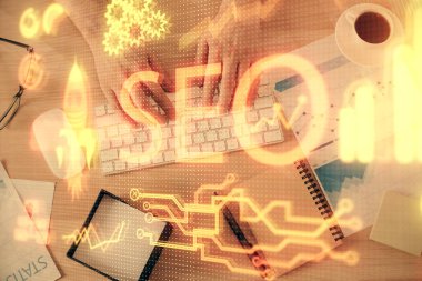 Bilgisayar klavyesinin ve SEO hologram çiziminin üzerine yazı yazan bir adamın eline çok kez maruz kalmış. Üst Manzara. Arama optimizasyon kavramı.