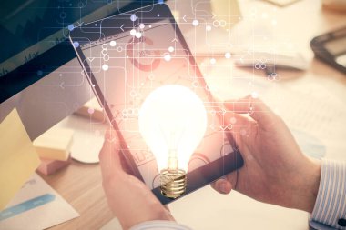 Dijital bir cihaz ve ampul hologram çizimi kullanarak insanın ellerini tutarken çift pozlama. Fikir kavramı.