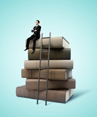 kitap yığını üzerinde oturan adam