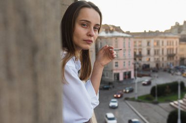 Genç ve güzel bir kız balkonda sigara içiyor, gün doğumunda, sağlıklı bir yaşam tarzı değil.