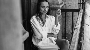 Siyah beyaz fotoğraf, balkonda sigara içen güzel bir kız, gün doğumu, sağlıklı bir yaşam tarzı değil.