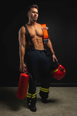 Kaslı, yakışıklı bir itfaiyecinin portresi koyu bir arka planda, elinde bir yangın kaskı, yana bakıyor.