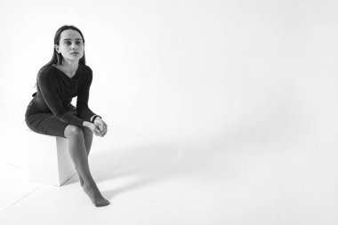 Beyaz kare bir sandalyede oturan genç, güzel bir kız, arka planda izole edilmiş, dik dik bakan, düşünceli, gerçekten. Yansıma kavramı. Seçici odaklanma. Siyah beyaz fotoğraf 