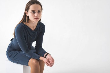 Beyaz bir meydanda oturan, beyaz bir arka planda soyutlanmış, düzgün, düşünceli, ciddi görünen genç, güzel bir ırk kızı.