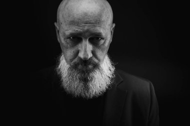 Yakın plan fotoğraf, ciddi, düşünceli, sakallı bir adamın karanlık arka planda kendine güveni ve dramatik bakışları. Erkek portresi kavramı. Siyah beyaz fotoğraf. Alçak tuş