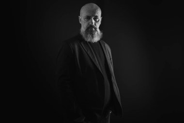 Yakın plan fotoğraf, ciddi, düşünceli, sakallı bir adamın karanlık arka planda kendine güveni ve dramatik bakışları. Erkek portresi kavramı. Siyah beyaz fotoğraf. Alçak tuş