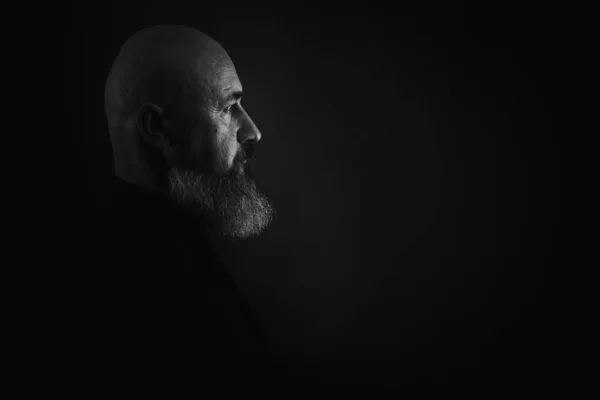 Yakın plan fotoğraf, ciddi, düşünceli, sakallı bir adamın karanlık arka planda kendine güvenen ve dramatik bir şekilde yana bakan portresi. Erkek portresi kavramı. Alçak tuş