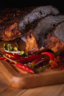Üst manzara, lezzetli, sulu ve güzel kokulu domuz eti, koyu bir arka planda tahta bir tahtada pirzola, acı kırmızı biber ve baharatlar. Lezzetli et konsepti