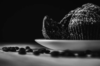 Siyah beyaz fotoğraf, sade anahtar, ev yapımı lezzetli çikolatalı kek, hamur işleri, ahşap bir yüzeyde beyaz bir kasede çörekler, yakın çekim. Lezzetli hamur işleri kavramı