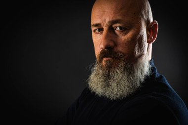 Yakın plan fotoğraf, ciddi, düşünceli, sakallı bir adamın karanlık arka planda kendine güveni ve dramatik bakışları. Erkek portresi kavramı. Alçak tuş 