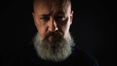 Yakın plan fotoğraf, ciddi, düşünceli, sakallı bir adamın karanlık arka planda kendine güveni ve dramatik bakışları. Erkek portresi kavramı. Alçak tuş 