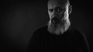 Yakın plan fotoğraf, ciddi, düşünceli, sakallı bir adamın karanlık arka planda kendine güveni ve dramatik bakışları. Erkek portresi kavramı. Siyah beyaz fotoğraf. Alçak tuş