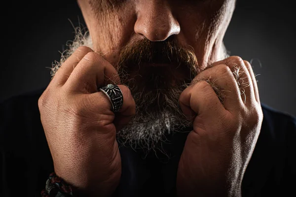 Frightened shocked worried bearded man, opened his mouth, holding his hands to his face, fingers in his beard, looking frightened in a panic, isolated on a dark background. Portrait, low key