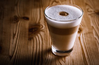Cafe latte macchiato katmanlı kahve, cam kahve fincanında. Kupa ahşap bir arka planda. Karanlık arka plan. Alçakgönüllülük. Seçici odak