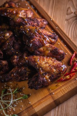 İştah açıcı, ızgarada pişirilmiş altın tavuk kanatları ahşap bir tahtada servis ediliyor, arka planda taze yeşillikler, üst manzara. Koyu arkaplan, düşük tuş