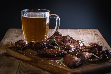 Yakın plan, yan görüş, bir bardak bira ve ahşap bir yüzey üzerinde kızarmış tavuk bacağı. Seçici odaklanma. Lezzetli et yemeği.