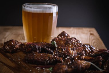 Yakın plan, yan görüş, bir bardak bira ve ahşap bir yüzey üzerinde kızarmış tavuk bacağı. Seçici odaklanma. Lezzetli et yemeği.