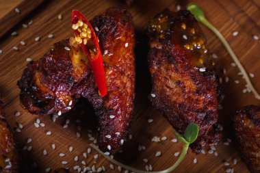 İştah açıcı, ızgarada pişirilmiş altın tavuk kanatları ahşap bir tahtada servis ediliyor, arka planda taze yeşillikler, üst manzara. Koyu arkaplan, düşük tuş