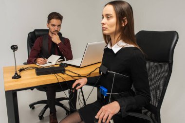 Konsantre, düşünceli bir kadın aydınlık bir odada, bir bilgisayar yalan makinesi üzerinde deneme yapıyor. Masada oturan genç adam yalan makinesi ve yalan makinesi monitörüne bakıyor. Doğruluk kavramı, yalan makinesi.