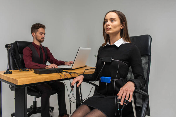 Concentrated, thoughtful woman is in a bright room, testing on a computer polygraph. Young man sitting at the table and looking at the polygraph screen and polygraph monitoring. The concept of truth, polygraph