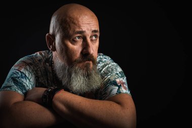 Vücut dili. Duygusal, yakın plan, duygusal, düşünceli, yakışıklı, sakallı genç bir iş adamının koluna yaslanmış portresi. Alçak tuş koyu arkaplanda izole edildi