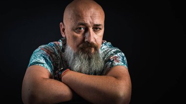 Vücut dili. Duygusal, yakın plan, duygusal, düşünceli, yakışıklı, sakallı genç bir iş adamının koluna yaslanmış portresi. Alçak tuş koyu arkaplanda izole edildi