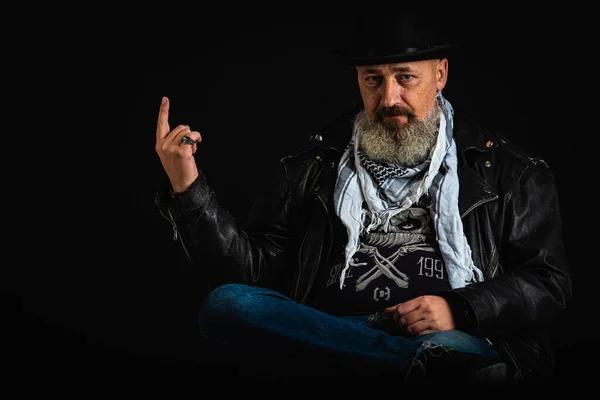 Body language, gestures, emotions. Cute, positive young bearded businessman, a man dressed in a dark leather smoker with a man\'s hat on his head, gesturing chickens. Low key. selective focus
