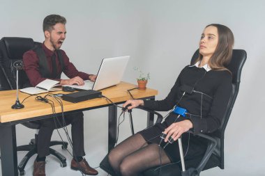 Odaklanmış, düşünceli bir kadın aydınlık bir odada, bir bilgisayar yalan makinesi üzerinde deneme yapıyor. Genç bir adam masada oturuyor ve genç bir işçi onu test ediyor ve ona bağırıyor. Yalan makinesi ve yalan makinesi izleme