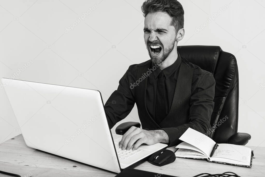 young handsome, focused man, businessman with beard, sitting working at desk near laptop at workplace bright office, writing e-mail, searching for information
