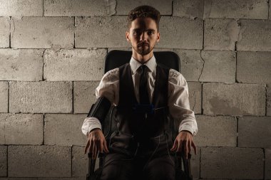 Konsantre, dalgın, gri bir odada sandalyede oturan, yalan makinesini test eden, yalan makinesini geçmek için algılayıcıları olan, gri tuğlalı bir arka planda oturan bir adam. Doğruluk kavramı, yalan makinesi.