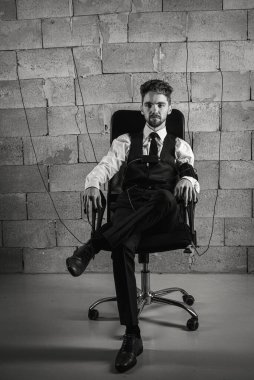 Endişeli, dalgın, sandalyede oturan, yalan makinesini test eden, yalan makinesinden geçmek için sensör takan, gri tuğla duvar arka planında oturan, el ele tutuşan eller. Alçakgönüllülük. Seçici odak