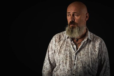 Yakın plan fotoğraf, ciddi, düşünceli, sakallı bir adamın karanlık arka planda kendine güvenen ve dramatik bir şekilde yana bakan portresi. Kavramsal erkek portresi. Alçak tuş
