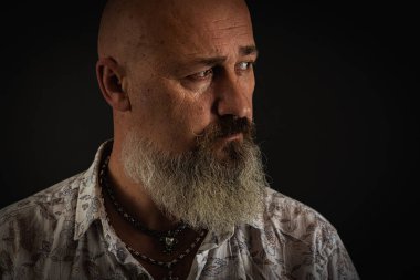 Yakın plan fotoğraf, ciddi, düşünceli, sakallı bir adamın karanlık arka planda kendine güvenen ve dramatik bir şekilde yana bakan portresi. Kavramsal erkek portresi. Alçak tuş